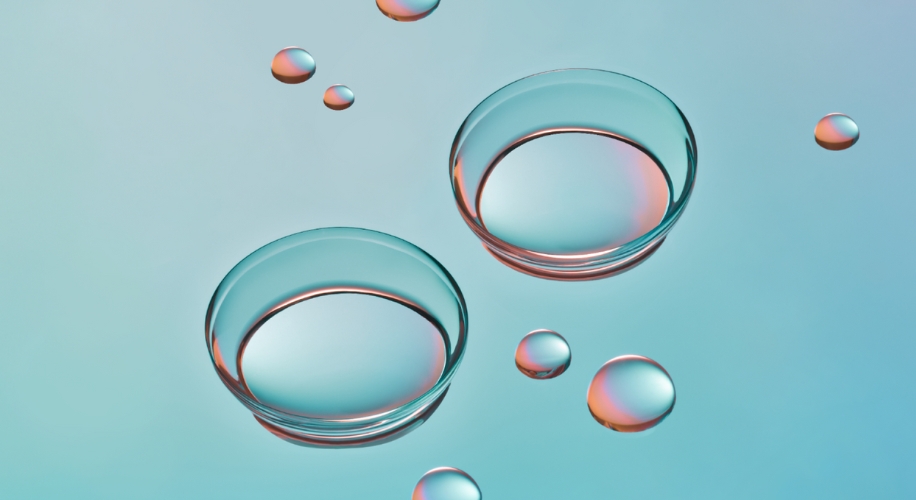 Two contact lenses and scattered water droplets on a turquoise background.