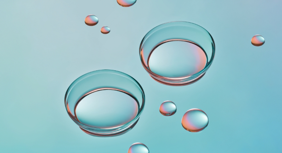 Two transparent contact lenses with water droplets on a teal background.