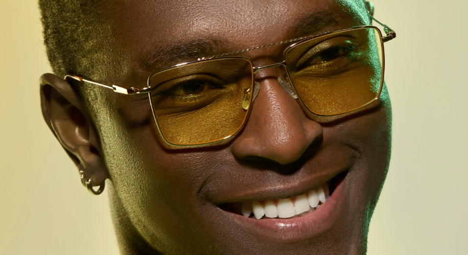 Man wearing gold-rimmed glasses with yellow-tinted lenses and a smile.