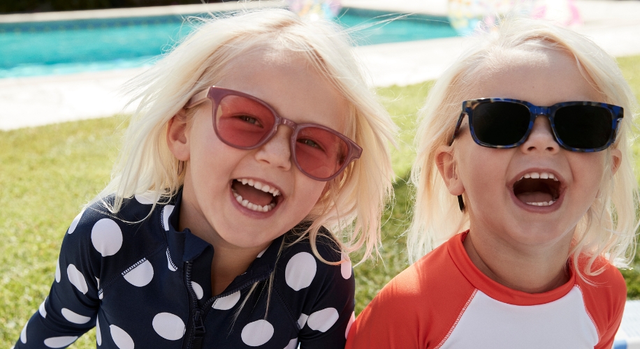 Children wearing UV-protective swimwear and sunglasses, smiling and playing near a pool.