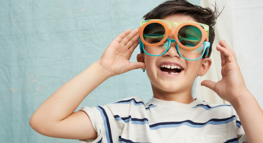 Child wearing oversized, colorful, double-layered goggles and a striped shirt, smiling and adjusting the goggles.