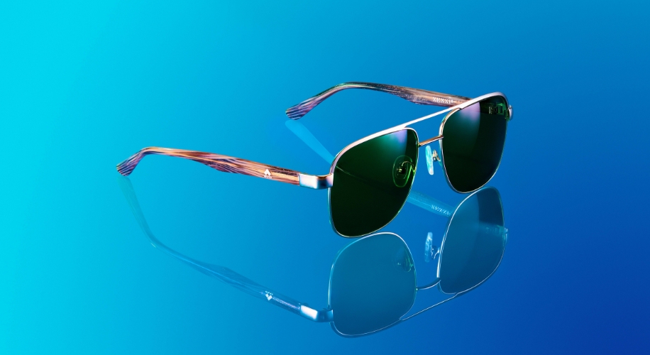 Sunglasses with green lenses and patterned brown frames, reflecting on a blue surface.