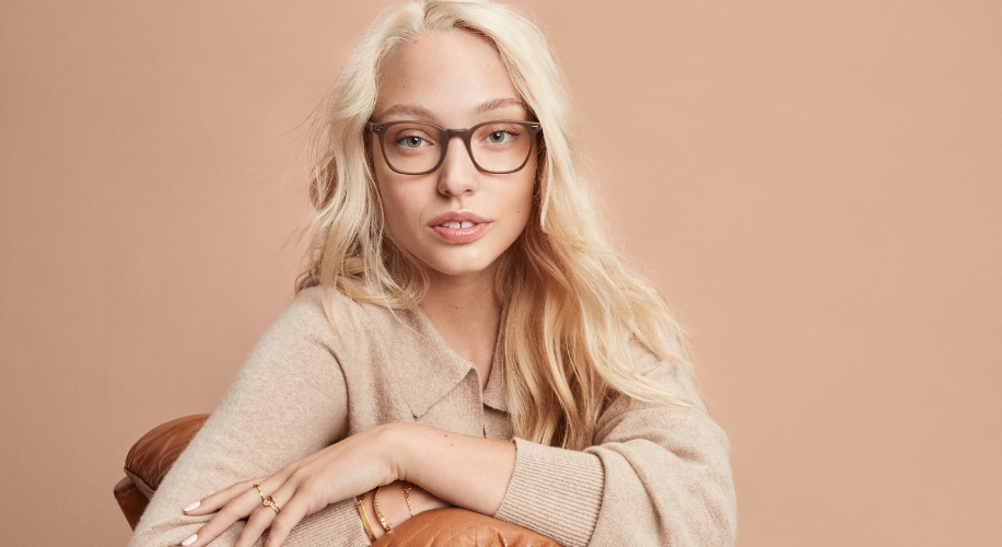 Woman wearing brown-framed eyeglasses and a beige sweater.