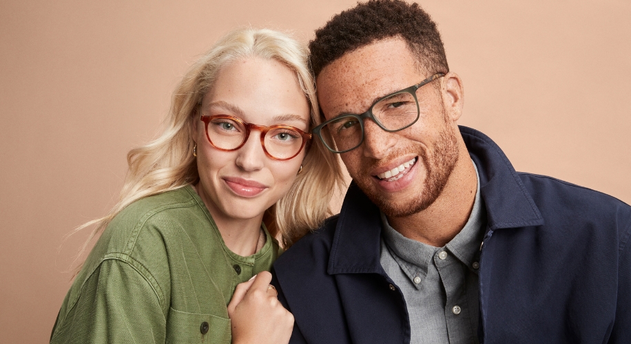 Two people wearing stylish eyeglasses: one with round red frames, the other with square green frames.