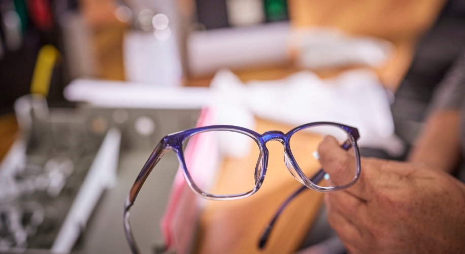 Blue-tinted eyeglasses being held by a person&#039;s hand.