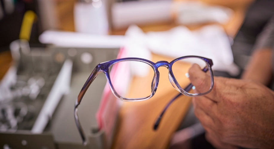 Person holding a pair of eyeglasses with a blue and transparent frame.