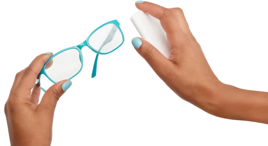 Blue-rimmed eyeglasses being sprayed with lens cleaner held by hand with matching blue nails.