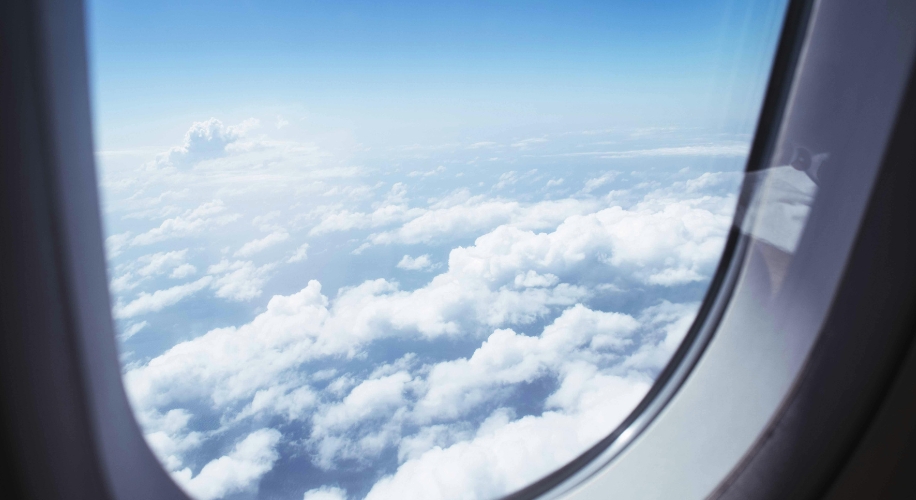 View of fluffy clouds and blue sky through an airplane window.