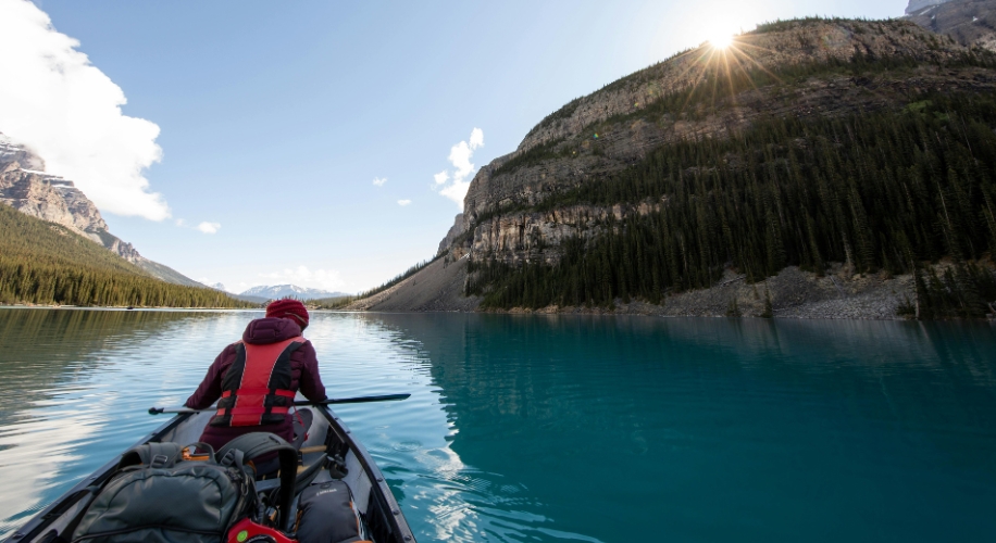 Person rowing a canoe on a turquoise lake surrounded by mountains.