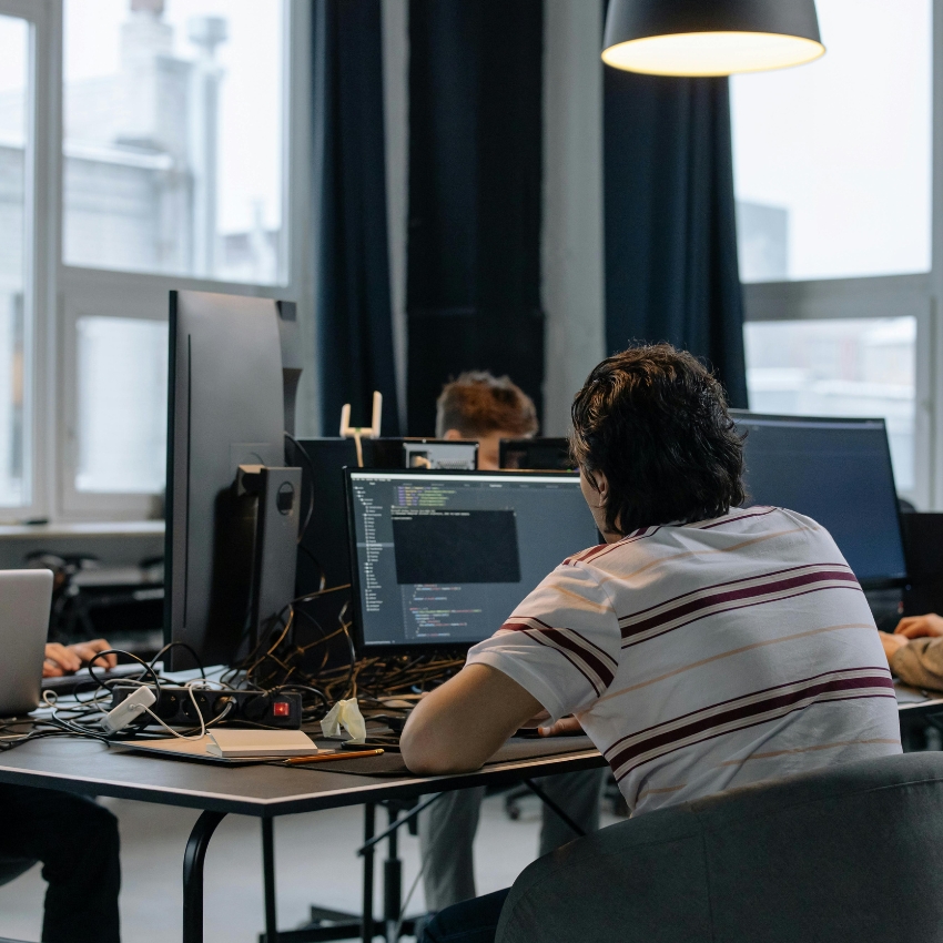 A person coding on a computer with multiple monitors on a desk.