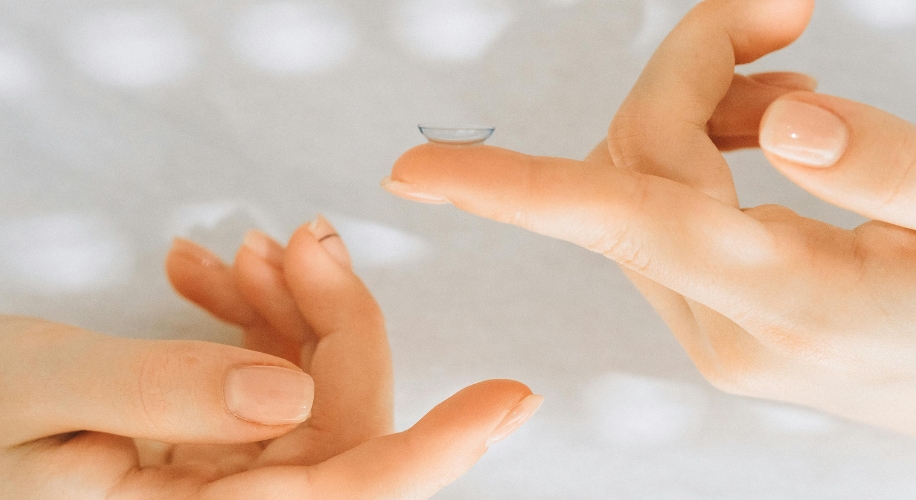 Contact lens balanced on fingertip, with another hand preparing to pick it up.