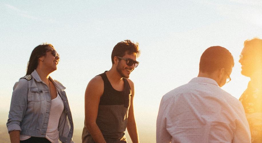 Group of people outdoors, smiling and talking, dressed in casual summer clothing.