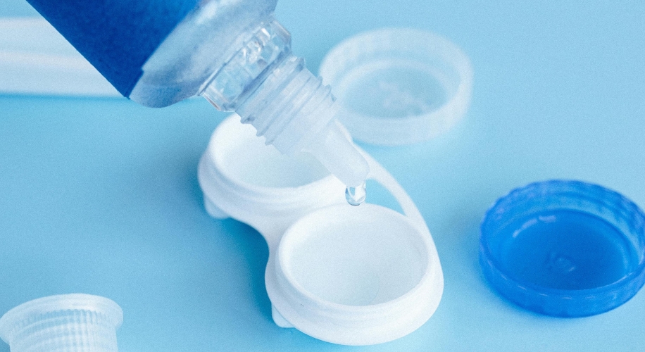 Contact lens solution bottle dispensing liquid into an open white contact lens case.