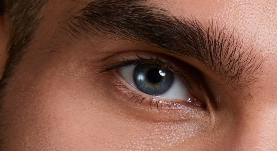 Close-up of a human eye with blue iris and thick eyebrows.