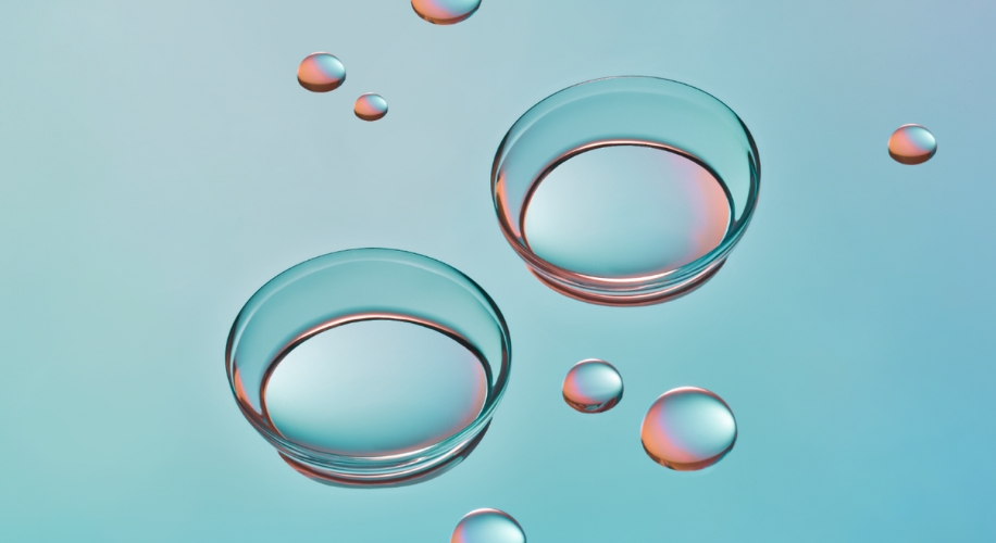 Two transparent contact lenses surrounded by small water droplets on a blue background.