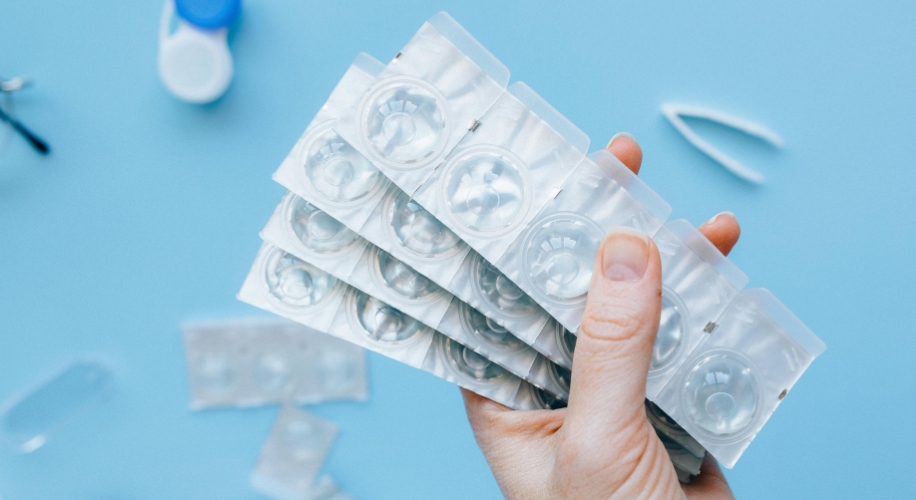 Hand holding blister packs of contact lenses against a blue background.