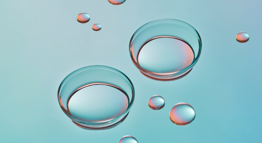 Two transparent contact lenses with reflection floating on a light blue background with small water droplets.