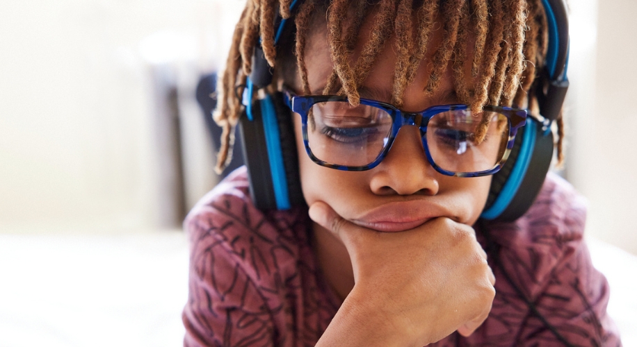 Child wearing blue over-the-ear headphones and large blue glasses with a contemplative expression.