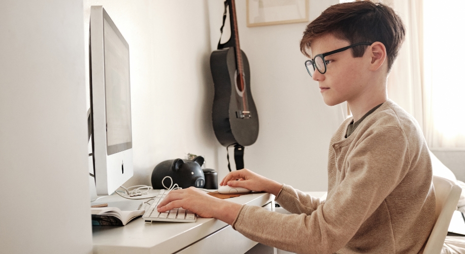 Child using an iMac computer at a white desk with a keyboard and mouse.