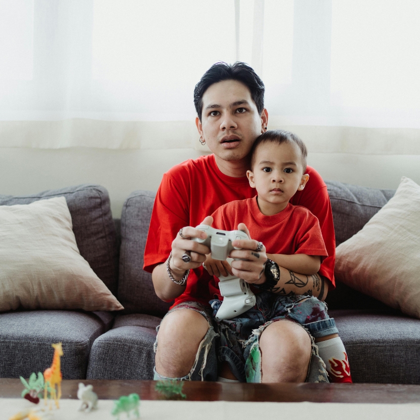 Adults and child wearing red shirts holding a game controller on a gray couch.