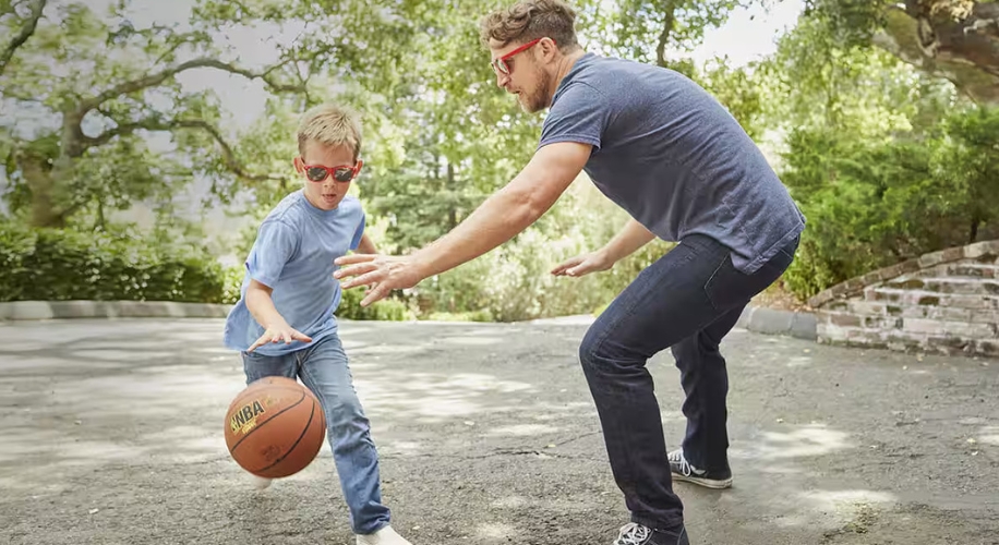 Adult and child playing basketball wearing red sunglasses. Spalding NBA basketball in mid-dribble.