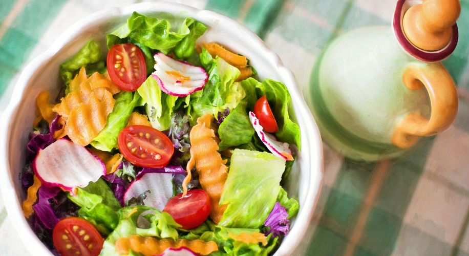 Fresh salad with mixed greens, cherry tomatoes, radish slices, and crinkle-cut carrots in a white bowl.