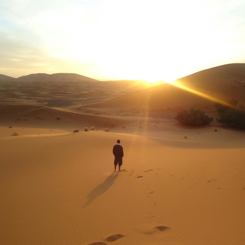 Person standing on desert sand dunes at sunset.