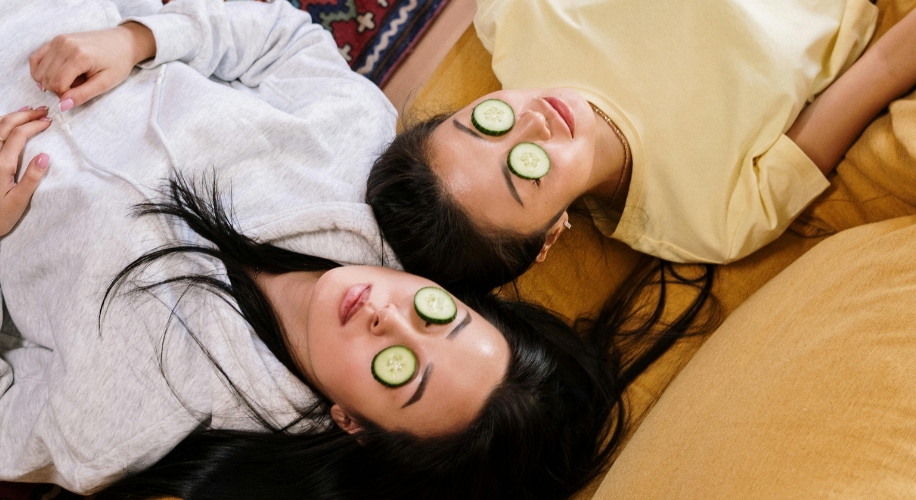 Two people lying down with cucumber slices covering their eyes.