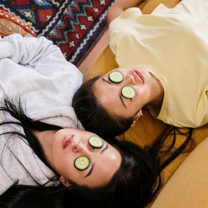 Two women lying with cucumber slices placed on their eyes.