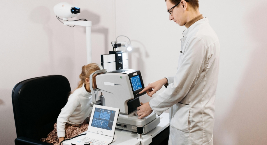 Optometrist using a digital refractor to examine a patient’s vision. The screen displays visual test data.