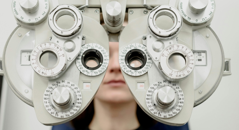 Phoropter used for eye exams, consisting of multiple dials and lenses, with a person looking through it.