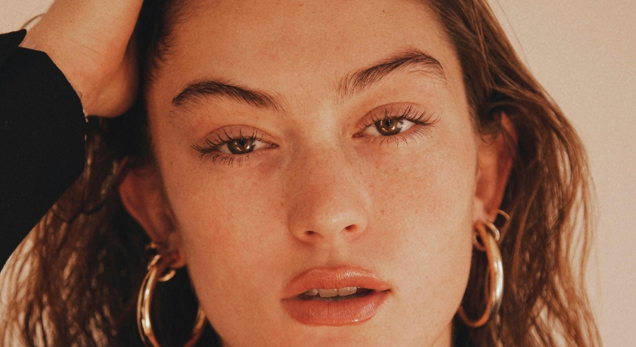 Woman wearing large gold hoop earrings and natural makeup, gently touching her hair.