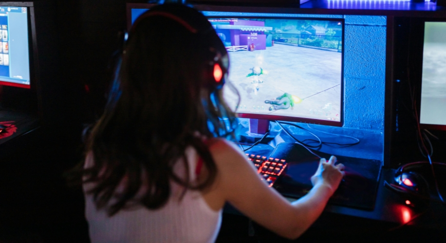 Person using a computer with a gaming headset, playing a video game on a brightly lit screen.