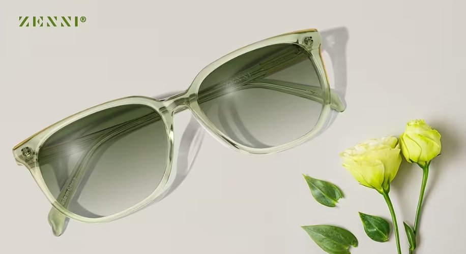 Zenni green translucent sunglasses with dark lenses, next to two yellow flowers with green leaves.