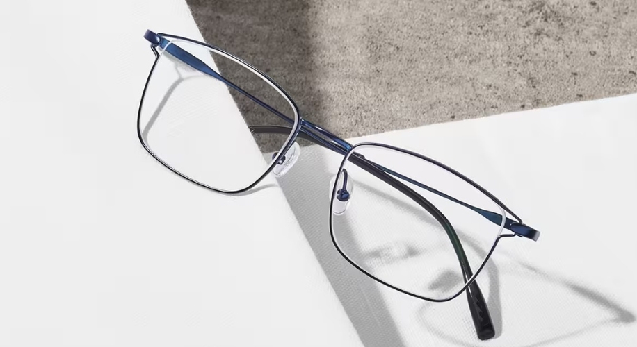 Thin, rectangular, metal-framed eyeglasses with dark blue and silver accents, sitting on a white surface.