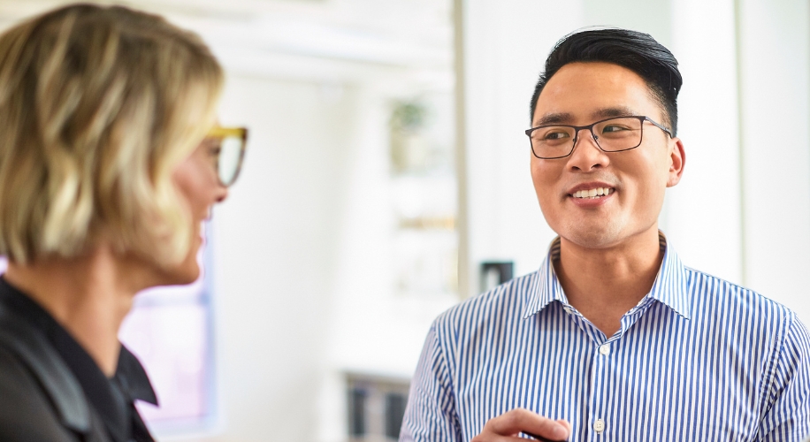 Man in striped shirt wearing glasses, smiling and talking to a woman with short blonde hair and glasses.