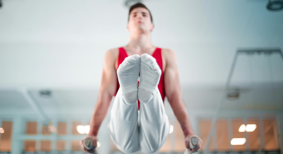 Gymnast in white outfit performing a L-sit on parallel bars.