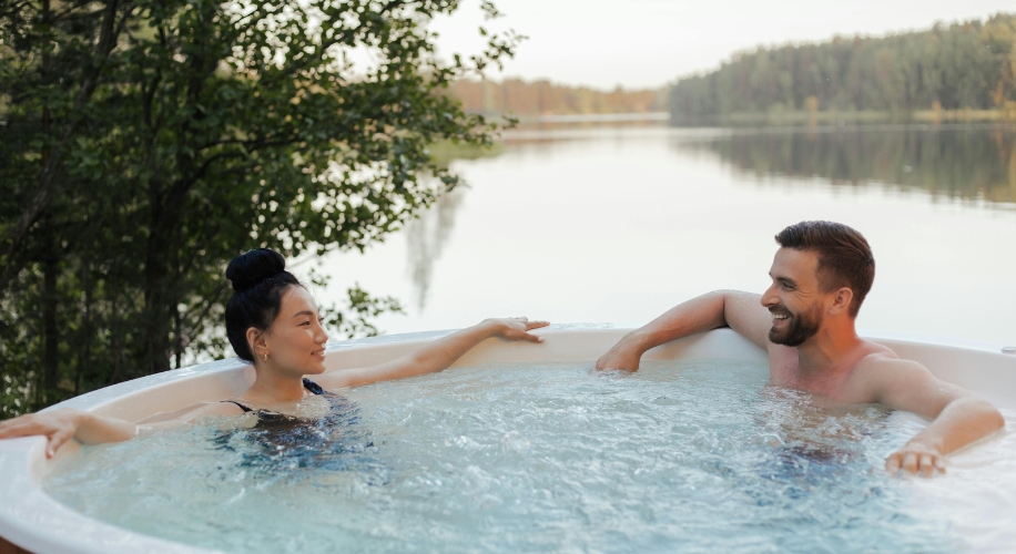 Couple relaxing in a hot tub by a serene lake.