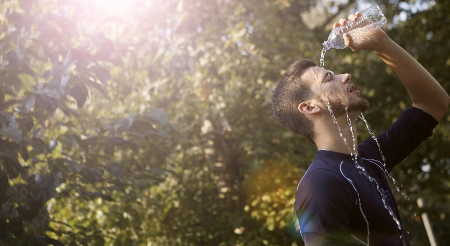 Man cooling off with water from a clear bottle.