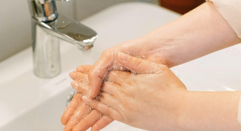 Hands being washed with soap under a running faucet.