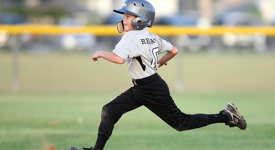 Child in a baseball uniform running. The shirt says &quot;Reagan&quot; and &quot;10.&quot; Wearing a helmet and cleats.