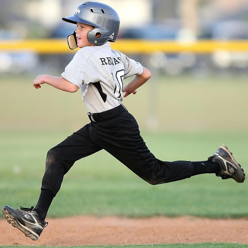 Young boy playing baseball, wearing helmet and jersey with number 10 and name "REAV." Running on field.