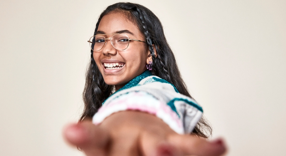 Smiling girl wearing eyeglasses and a sweater with green and pink patterns.