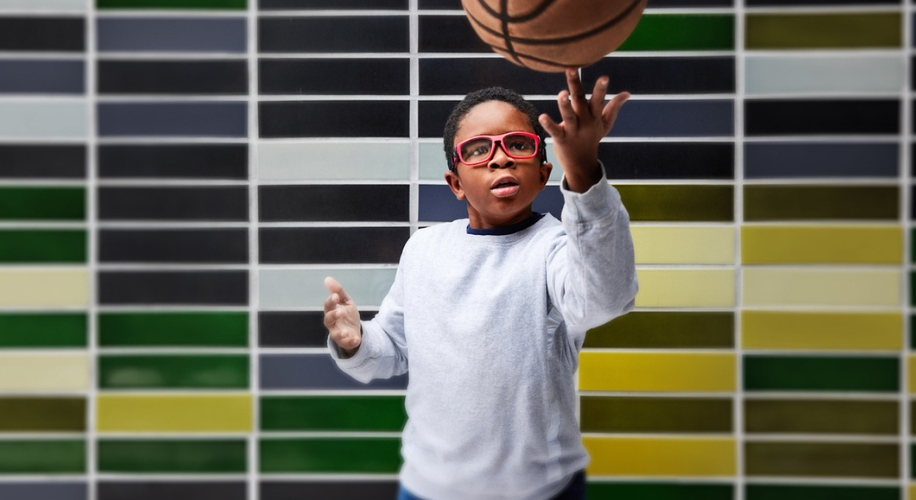 Boy with red-framed glasses and grey sweater skillfully spinning a basketball.