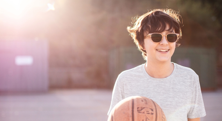 Smiling person with short hair, wearing sunglasses, holding a basketball.