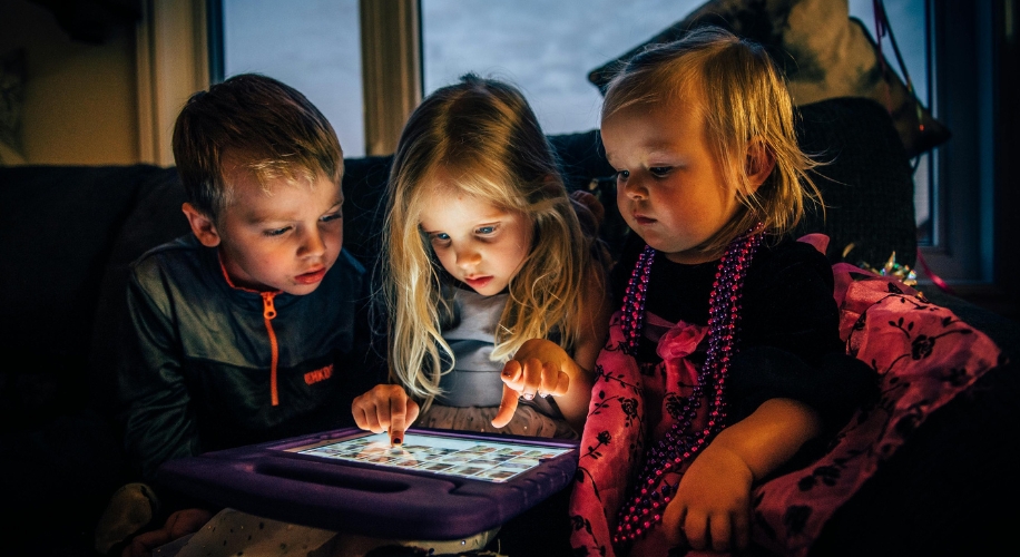 Three children using a tablet with a purple case, one child is touching the screen with curiosity.