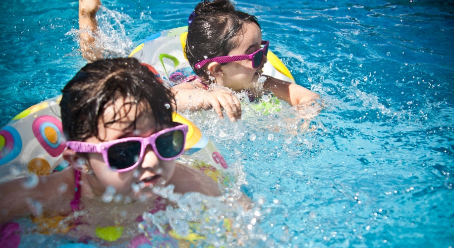 Kids wearing sunglasses and colorful swim rings playing in the pool.