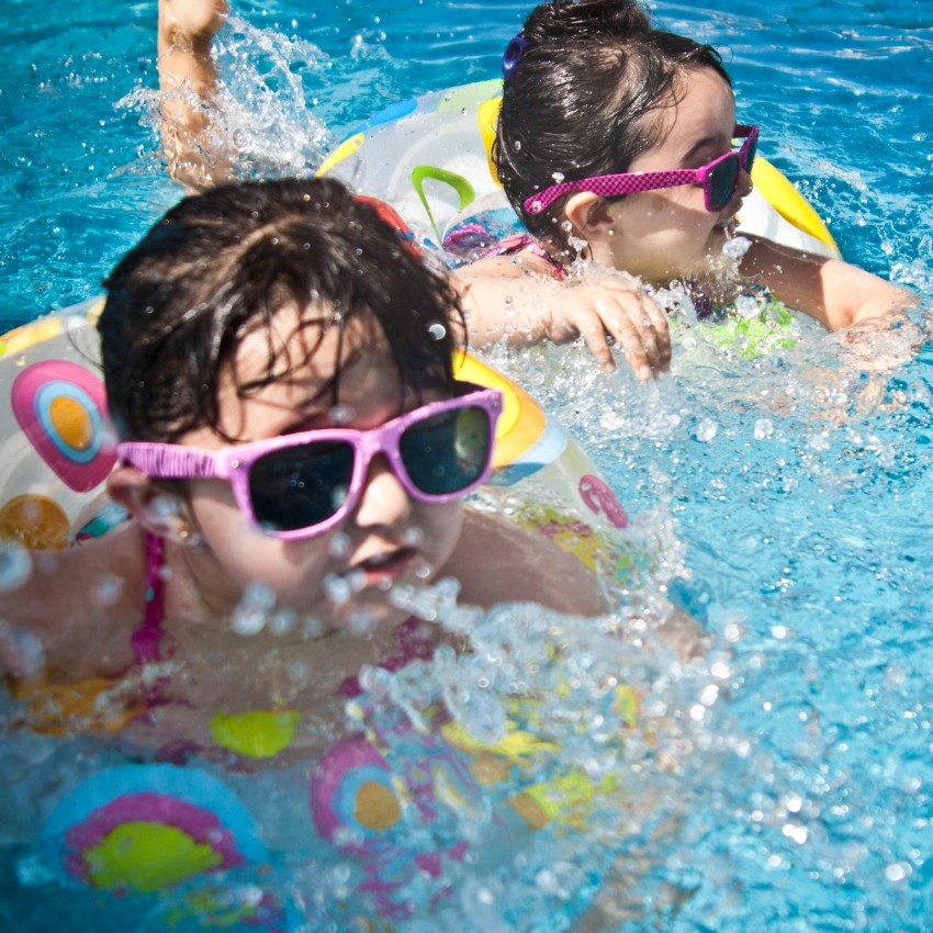 Children wearing colorful sunglasses swimming in a pool with patterned inflatable rings.