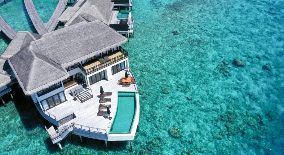 Beachfront overwater villa with private pool, sun loungers, and outdoor dining area over turquoise water.