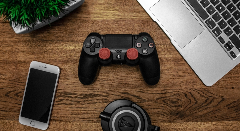 Black gaming controller with red joystick covers on a wooden surface.